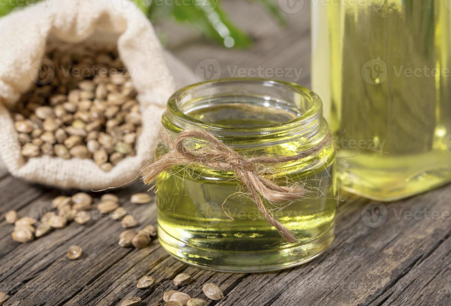 aceite de cáñamo de primer plano en frasco de vidrio y botella con granos de cannabis en saco sobre tabla de madera. foto