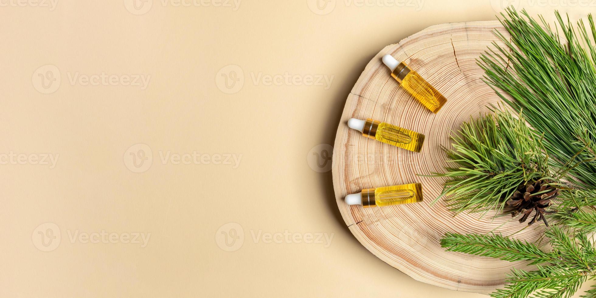 Three small glass bottles with coniferous essential oils of pine, spruce and cedar with branches on wooden cut on beige. photo