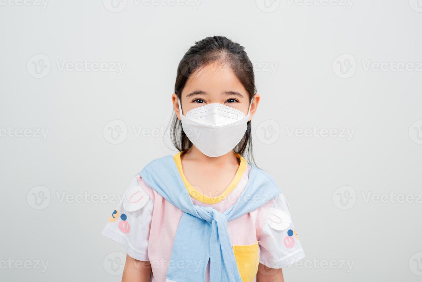 Asian little child girl wearing respirator mask to protect coronavirus outbreak and pointing hand to blank background, New virus Covid-19 photo
