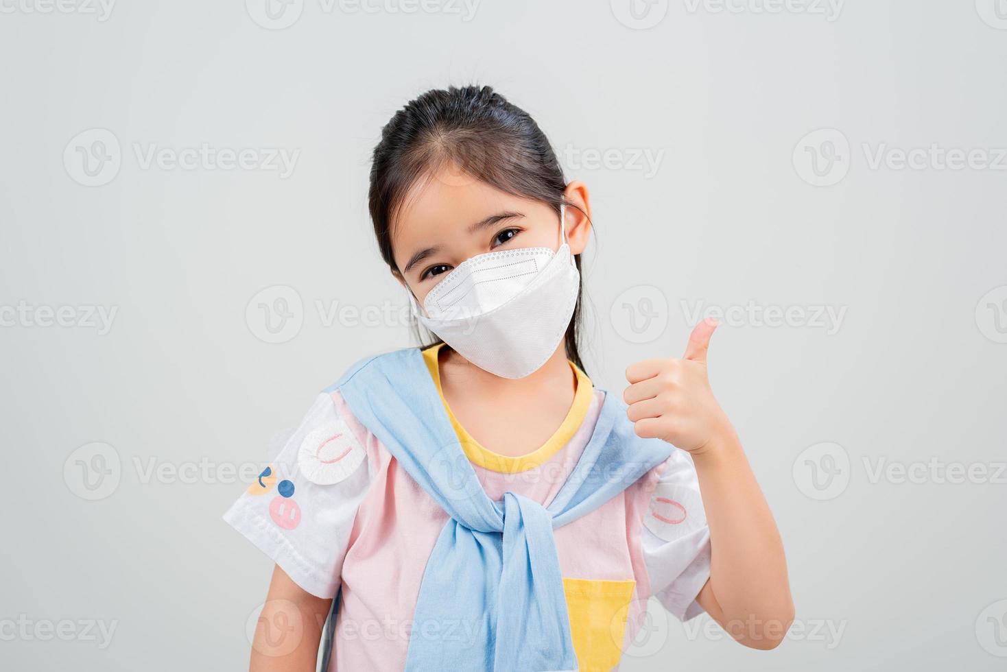 Asian little child girl wearing respirator mask to protect coronavirus outbreak and pointing hand to blank background, New virus Covid-19 photo