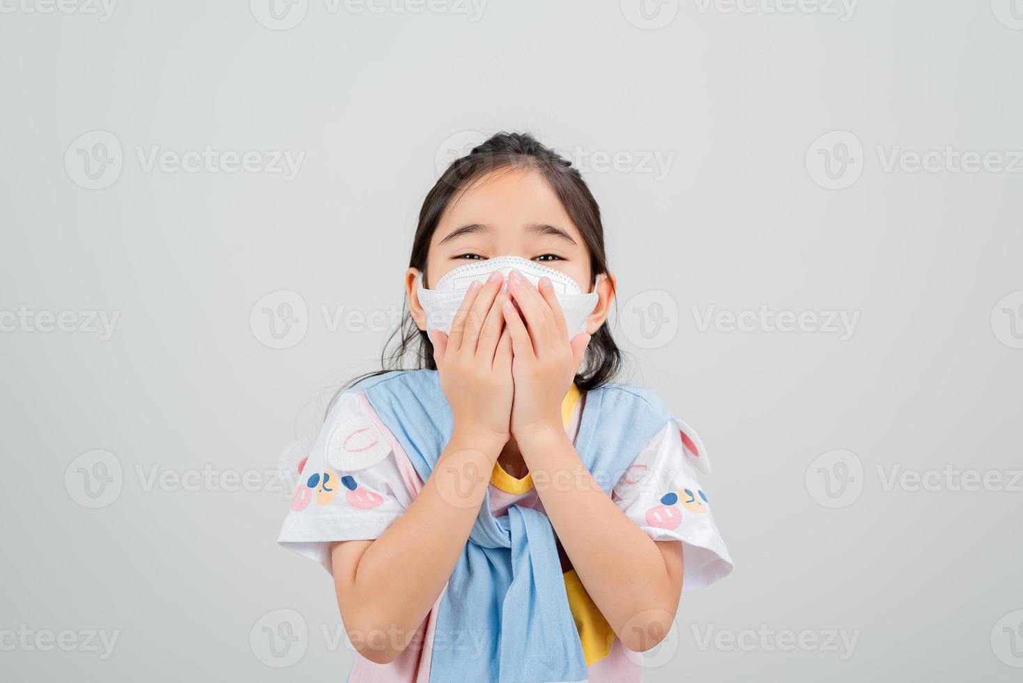 Asian little child girl wearing respirator mask to protect coronavirus outbreak and pointing hand to blank background, New virus Covid-19 photo