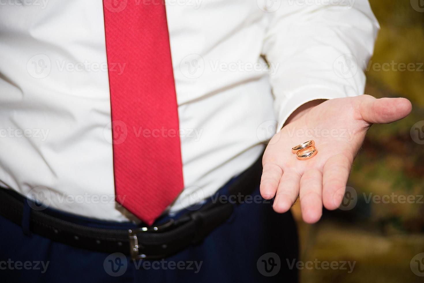 groom holds the wedding ring on his hand photo