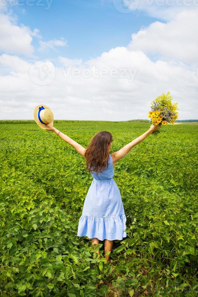 the girl is standing in the field with a bouquet of yellow flowers and a straw hat photo