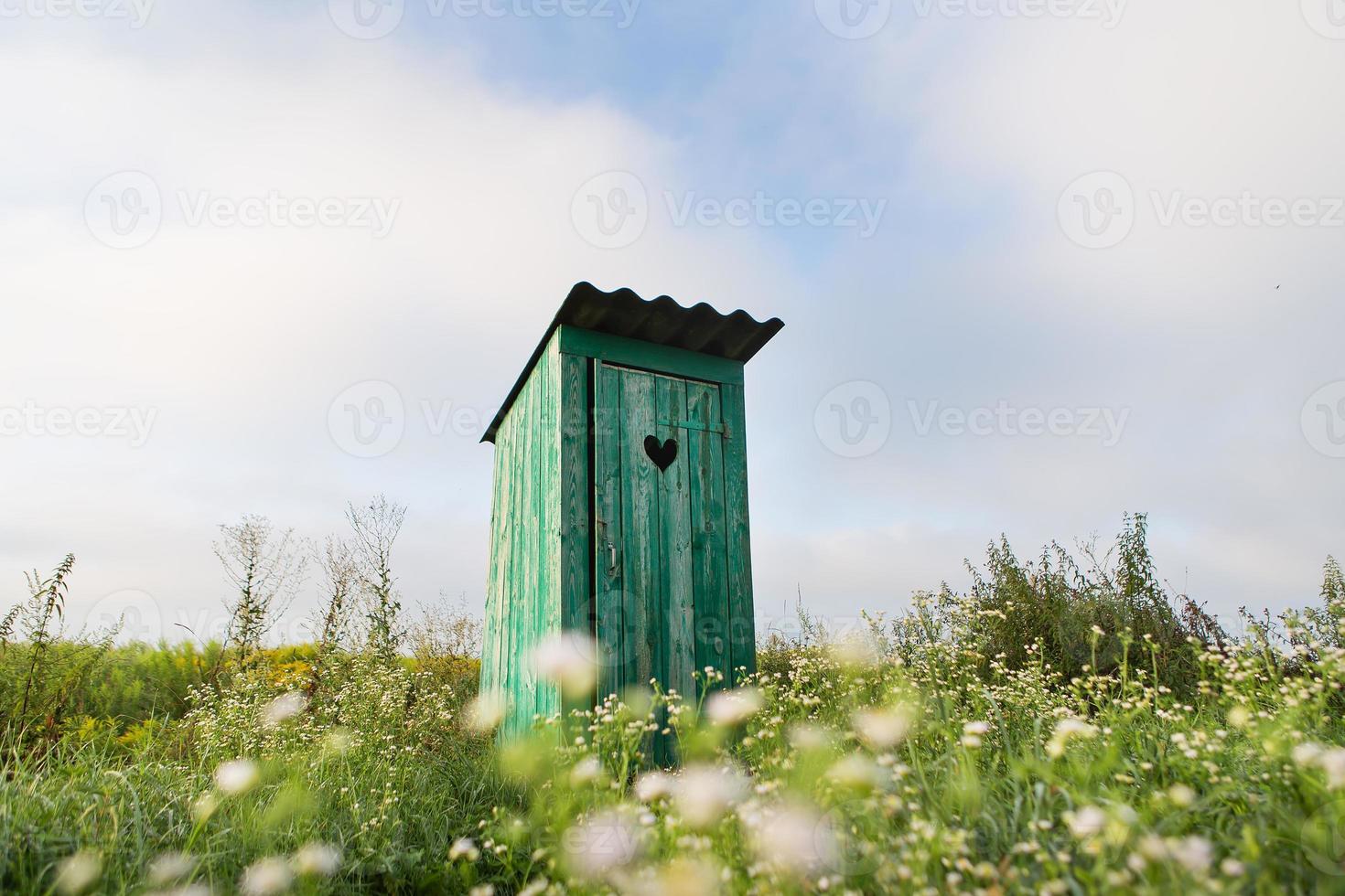 Vintage toilet. An outdoor rustic green toilet with a heart cut out on the door. Toilet in a field of flowers. photo