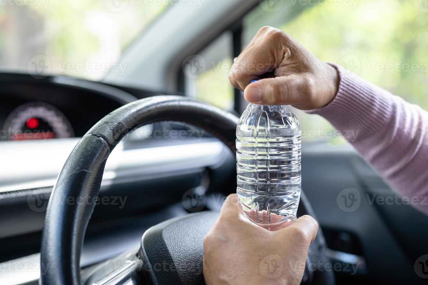 Asian woman driver holding bottle for drink water while driving a car