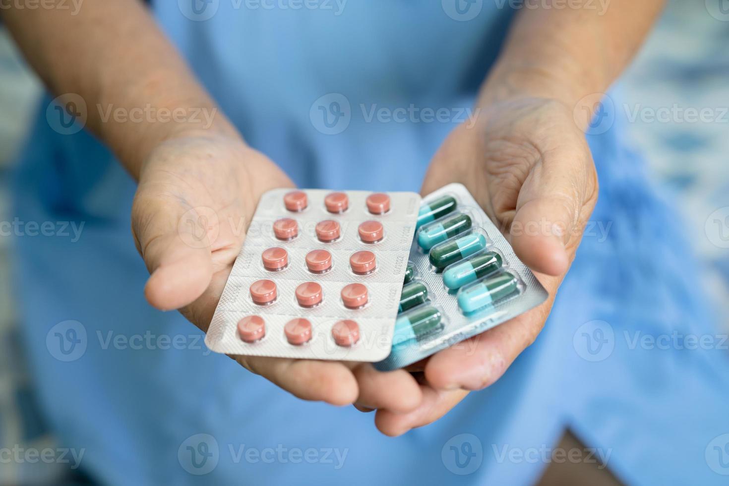 Asian senior or elderly old lady woman patient holding antibiotics capsule pills in blister packaging for treatment infection patient in hospital, Pharmacy drugstore concept. photo