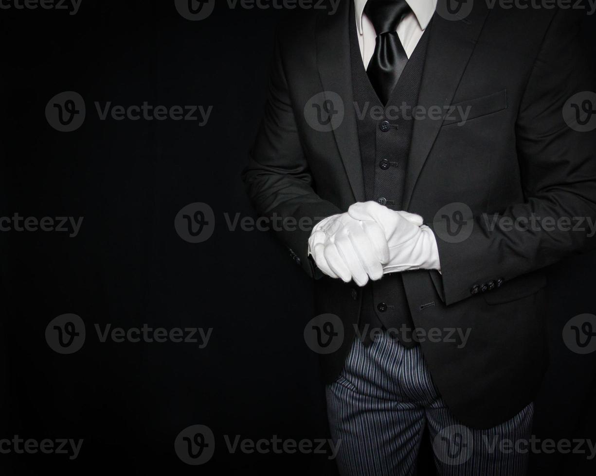 retrato de mayordomo o sirviente con traje oscuro y guantes blancos listos para ayudar con fondo negro. servicio Industrial. hospitalidad y cortesía profesional foto