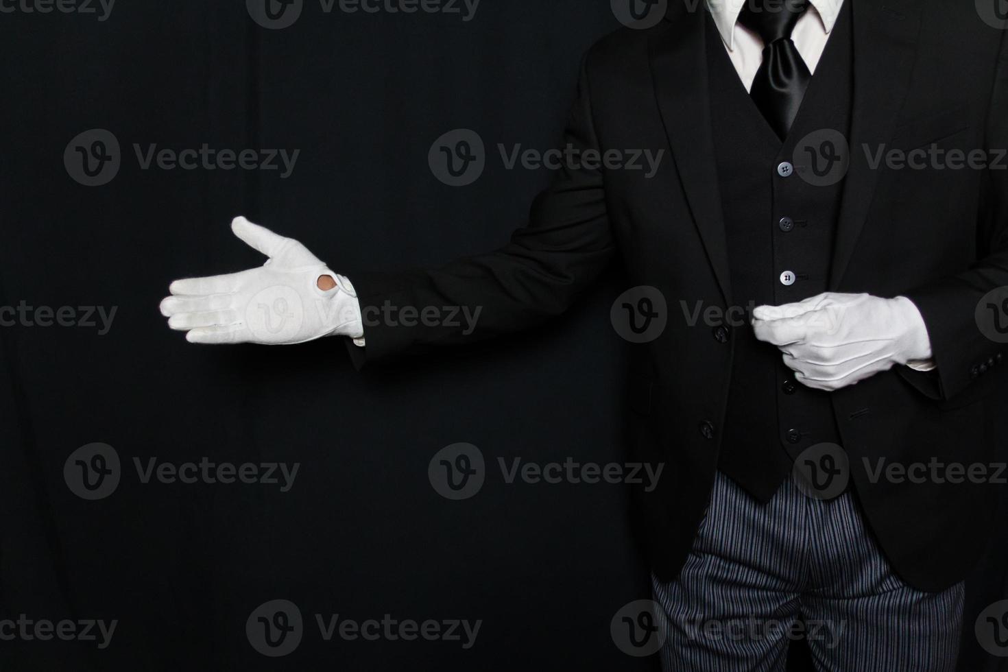 Portrait of Butler or Servant in Dark Suit and White Gloves with Welcoming Gesture on Black Background. Service Industry. Professional Hospitality and Courtesy. photo