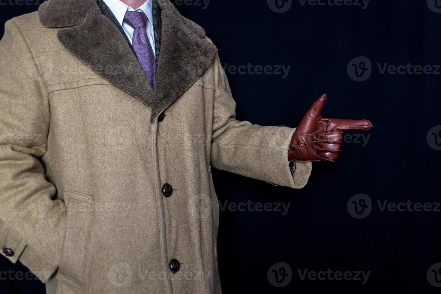 retrato de hombre con abrigo y traje con gesto de pistola en el dedo sobre fondo negro. película negra agente secreto espía héroe. detective luchando contra el crimen. foto