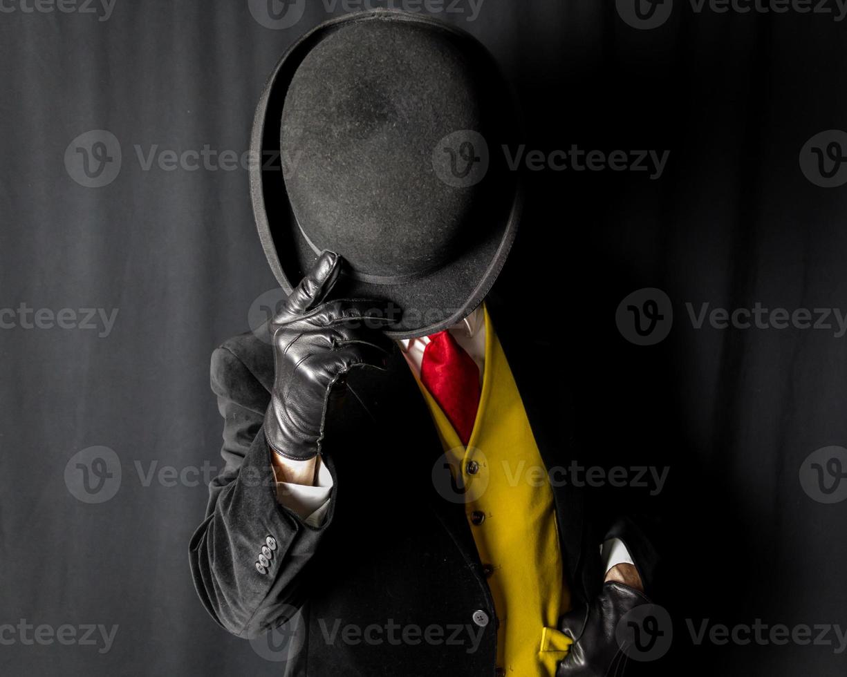 Portrait of Man in Dark Suit and Yellow Vest and Red Tie Holding Bowler Hat Over His Face photo