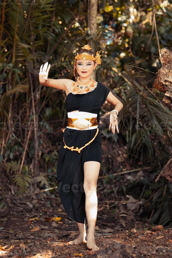 mujer javanesa bailando en una camiseta negra y falda negra con corona dorada y accesorios dorados en su cuerpo dentro de la jungla foto