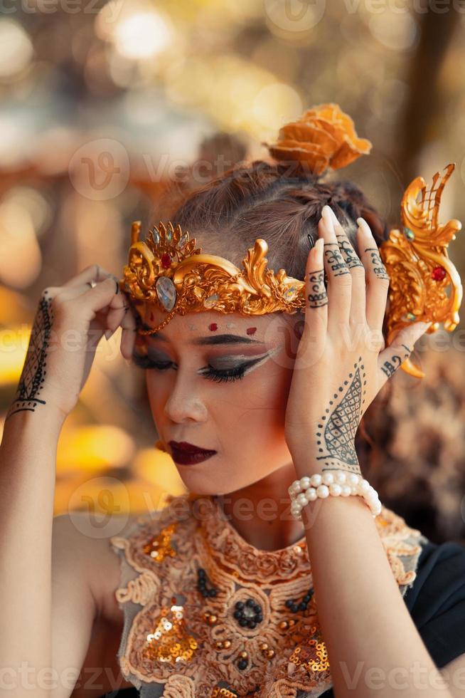 ancient woman in her golden crown and golden necklace pose in her black dress inside the forest photo