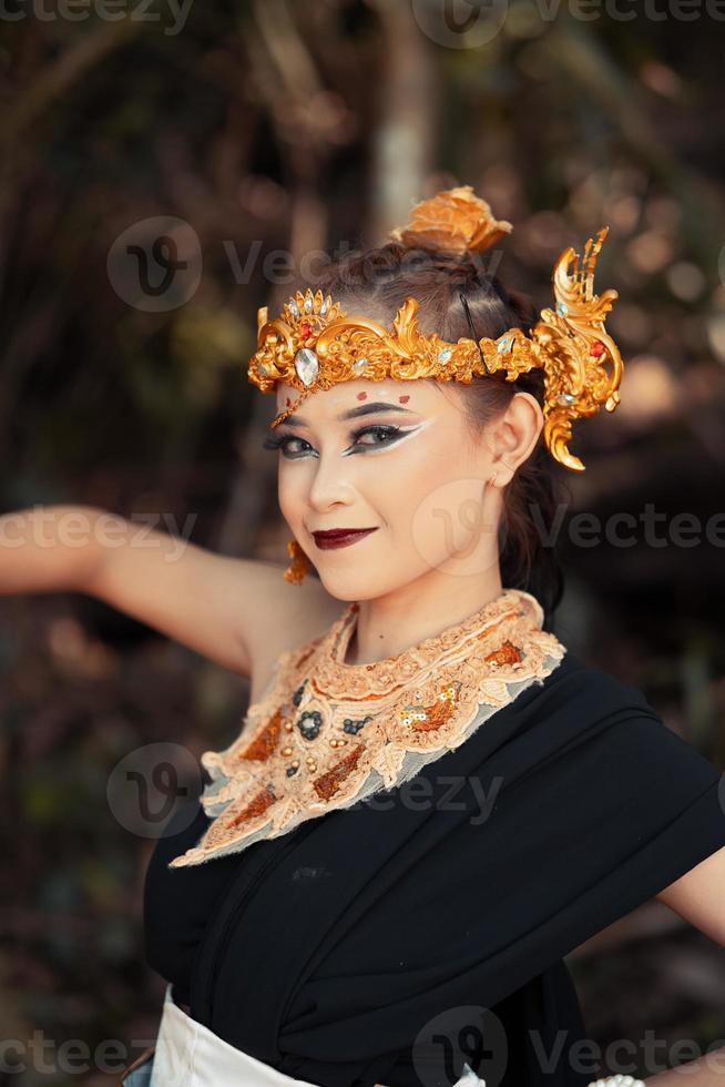 The face of an Asian woman with golden jewelry on her body while wearing a black costume with a happy face photo