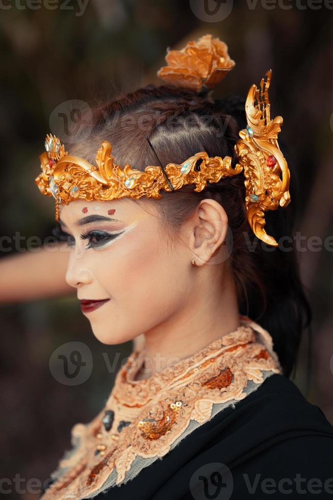 The face of an Asian woman with golden jewelry on her body while wearing a black costume with a happy face photo