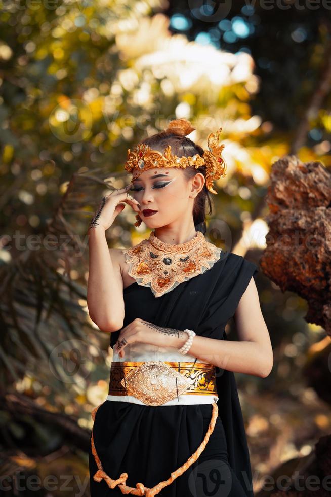 reina tribal maquillada mientras usa una corona de oro y un collar de oro con el vestido negro foto