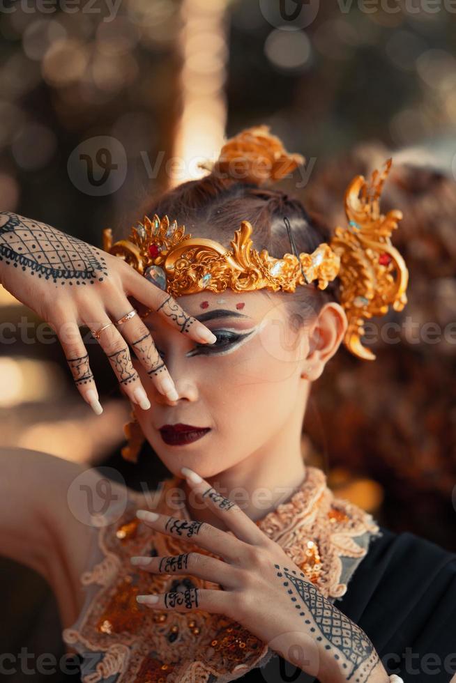 mujer exótica con su audaz maquillaje mientras usa accesorios dorados en la cabeza y el cuello con un vestido negro foto