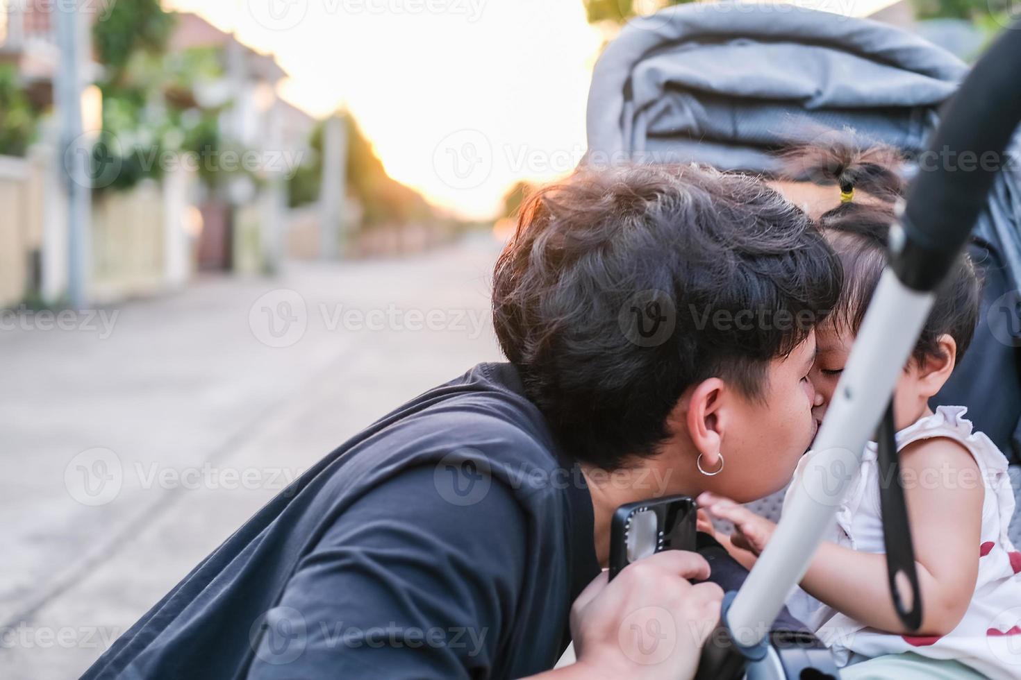 Asian father and daughter or son cute girl making kiss feeling happy and enjoy on baby stroller father and son eye contact smile so showing family love evening with sunlight on face happiness photo