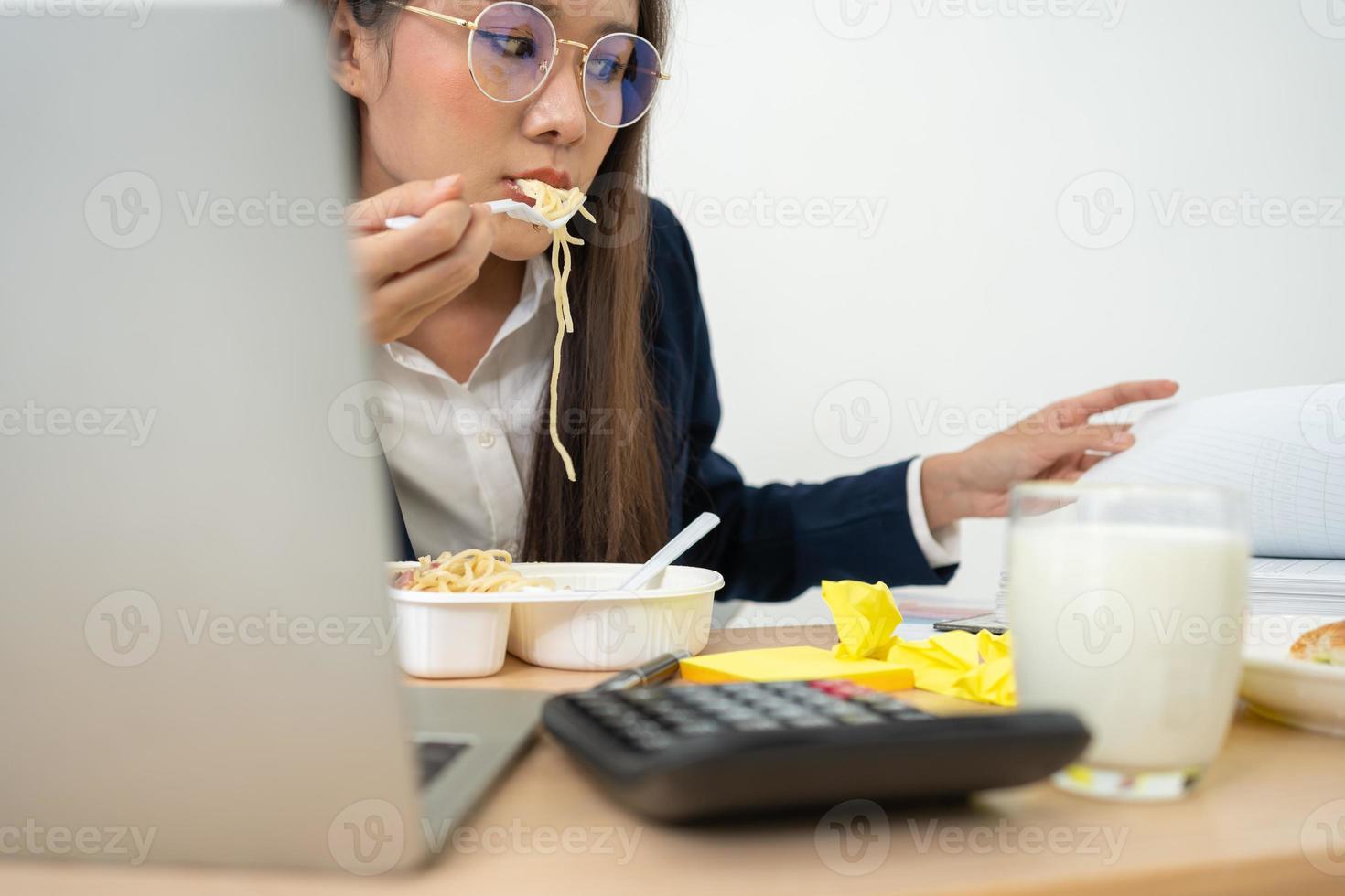 Busy and tired businesswoman eating spaghetti for lunch at the Desk office and working to deliver financial statements to a boss. Overworked and unhealthy for ready meals, burnout concept. photo