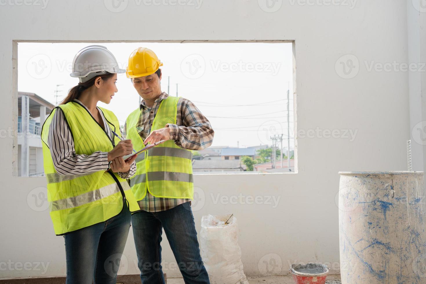 Asian engineer or Young Female Architect put on a helmet for safety and talk with a contractor on a construction building factory project, Concept of Teamwork, Leadership concept. photo