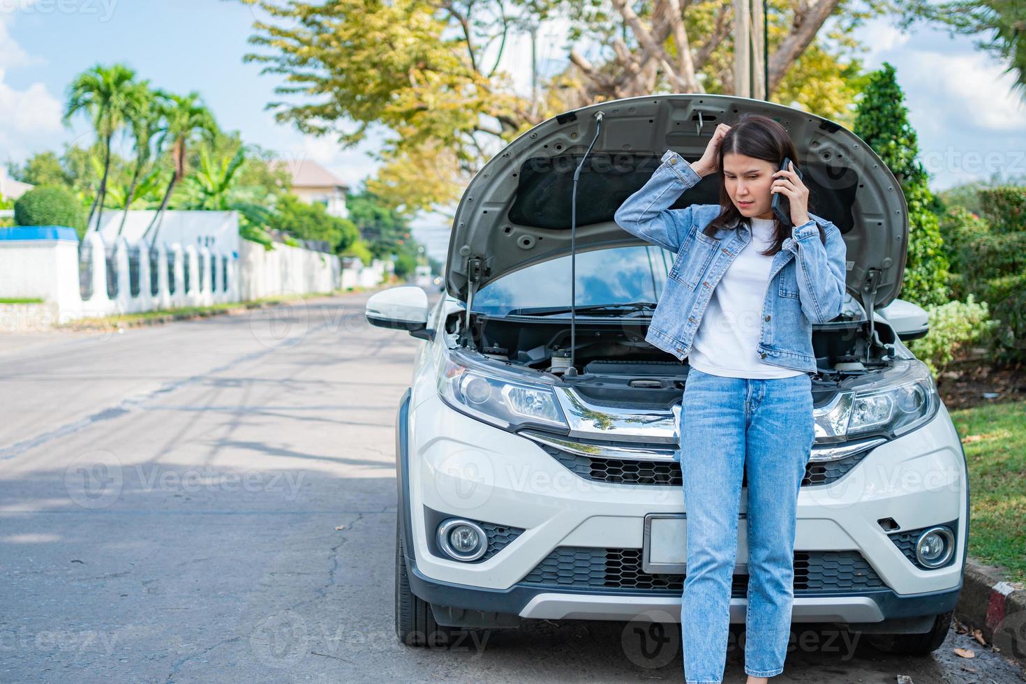 mujer asiática enojada y usando un teléfono móvil pidiendo ayuda después de una avería en el coche en la calle. concepto de problema del motor del vehículo o accidente y ayuda de emergencia de un mecánico profesional foto