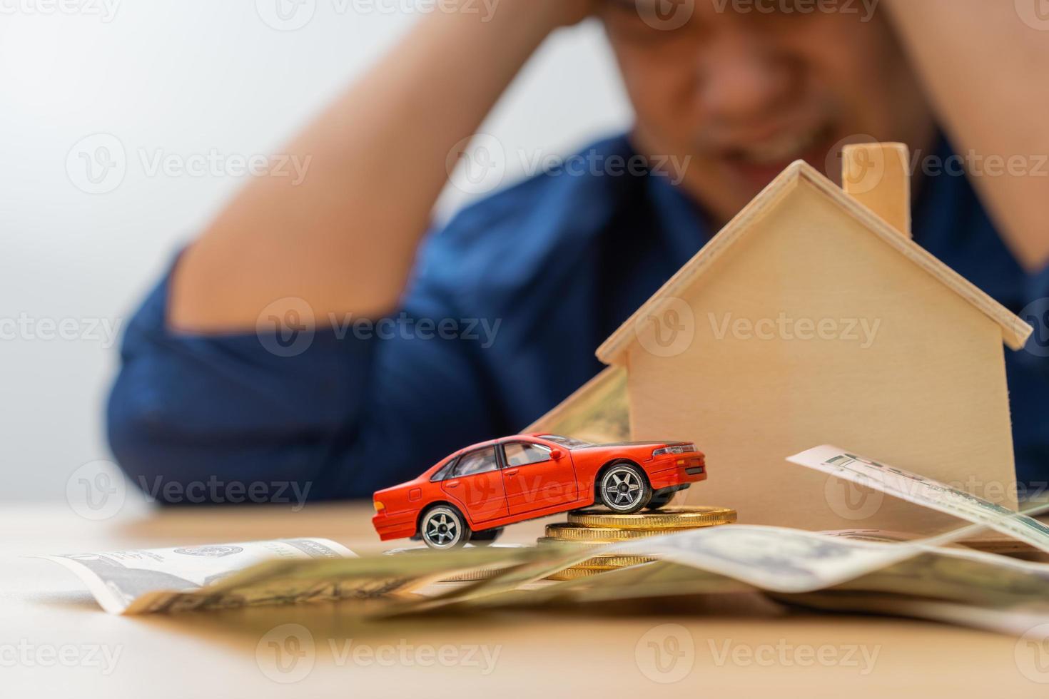 Unhappy Asian man holding a banknote and Making an account of income and expenses to pay the home loan and car loan, Concept loan payment and home insurance, economic problems, and inflation photo