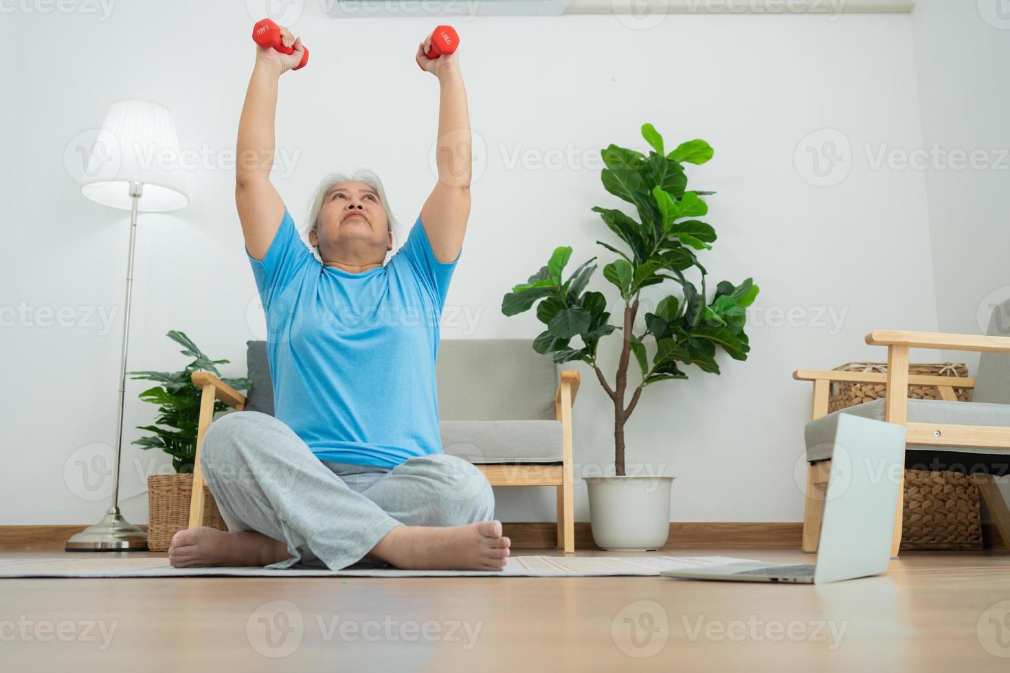 anciana asiática levantando pesas para hacer ejercicio y hacer ejercicio en casa. mujer madura activa haciendo ejercicio de estiramiento en la sala de estar. ejercicio activo y saludable para personas mayores, mayores y mayores. foto