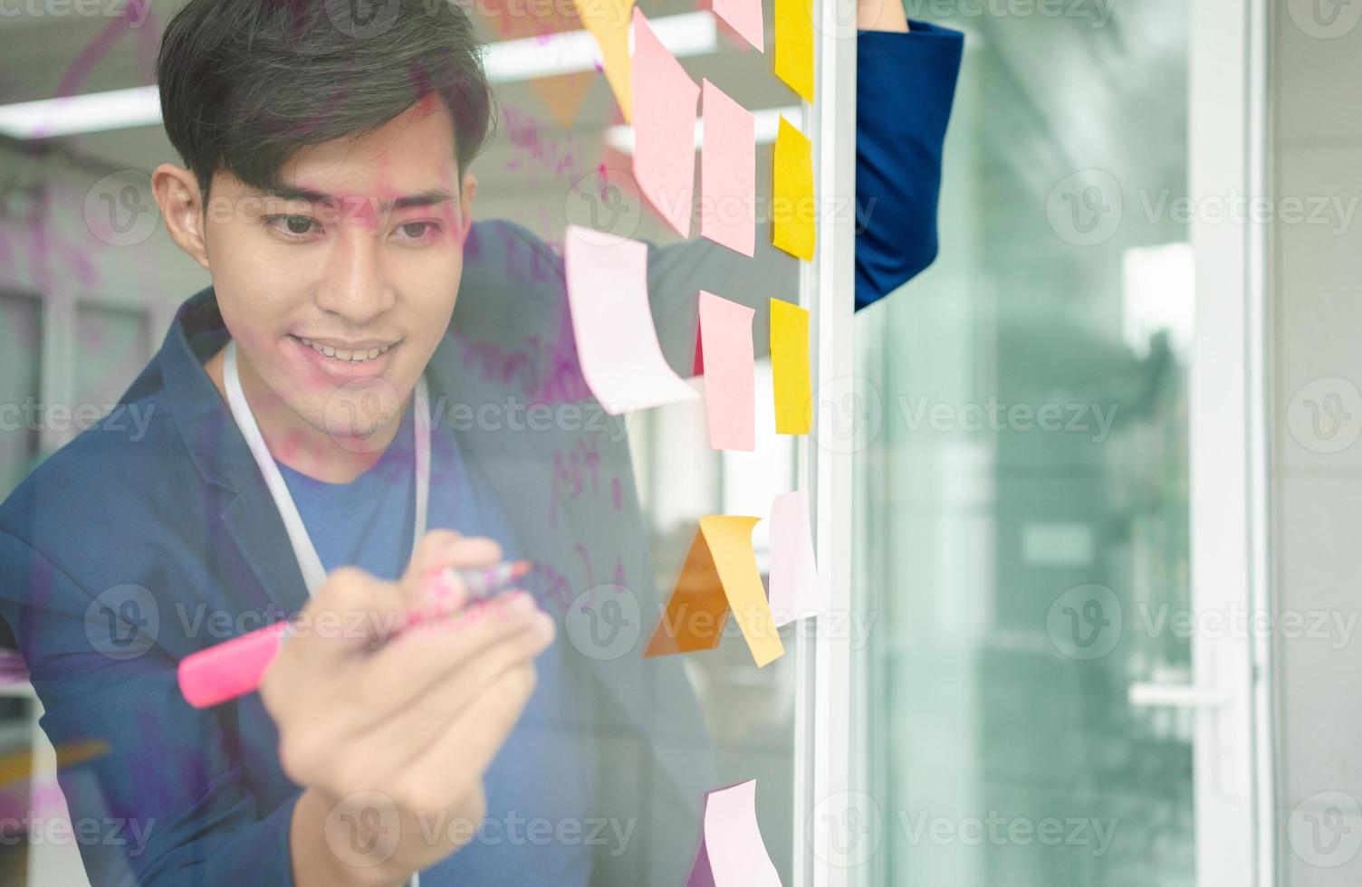 Young Creative businessman holding a marker and writing plan and share idea on glass wall with sticky note, Brainstorming and discussing and formulating, business strategies in tech startup office. photo