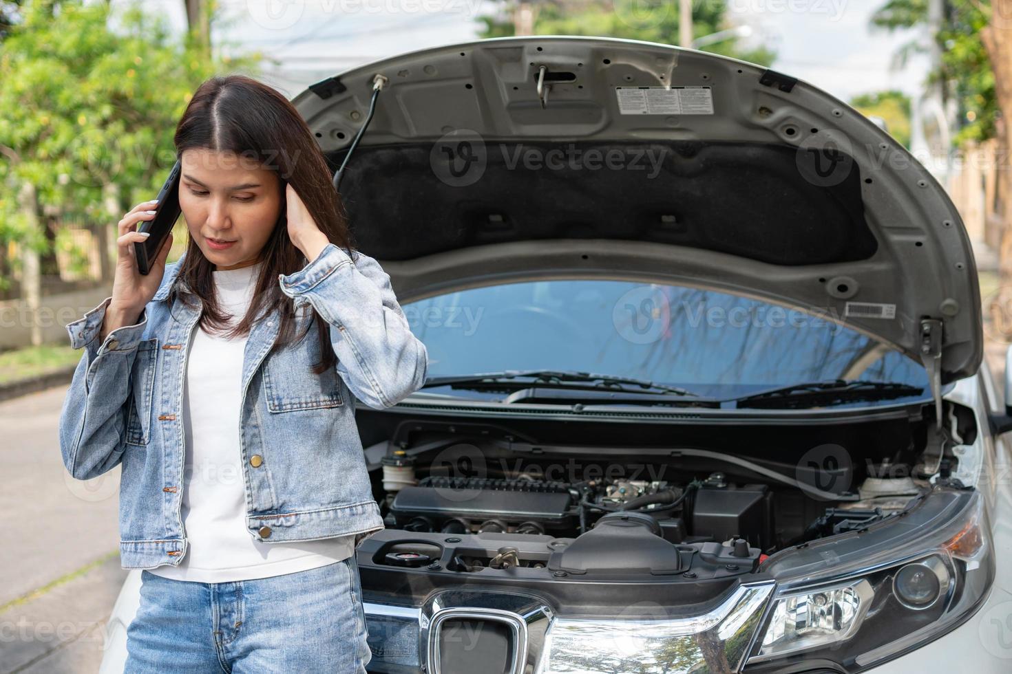 Angry Asian woman and using mobile phone calling for assistance after a car breakdown on street. Concept of vehicle engine problem or accident and emergency help from Professional mechanic photo