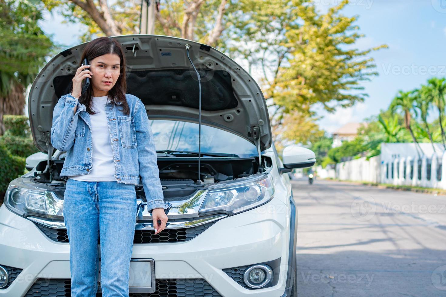 mujer asiática enojada y usando un teléfono móvil pidiendo ayuda después de una avería en el coche en la calle. concepto de problema del motor del vehículo o accidente y ayuda de emergencia de un mecánico profesional foto