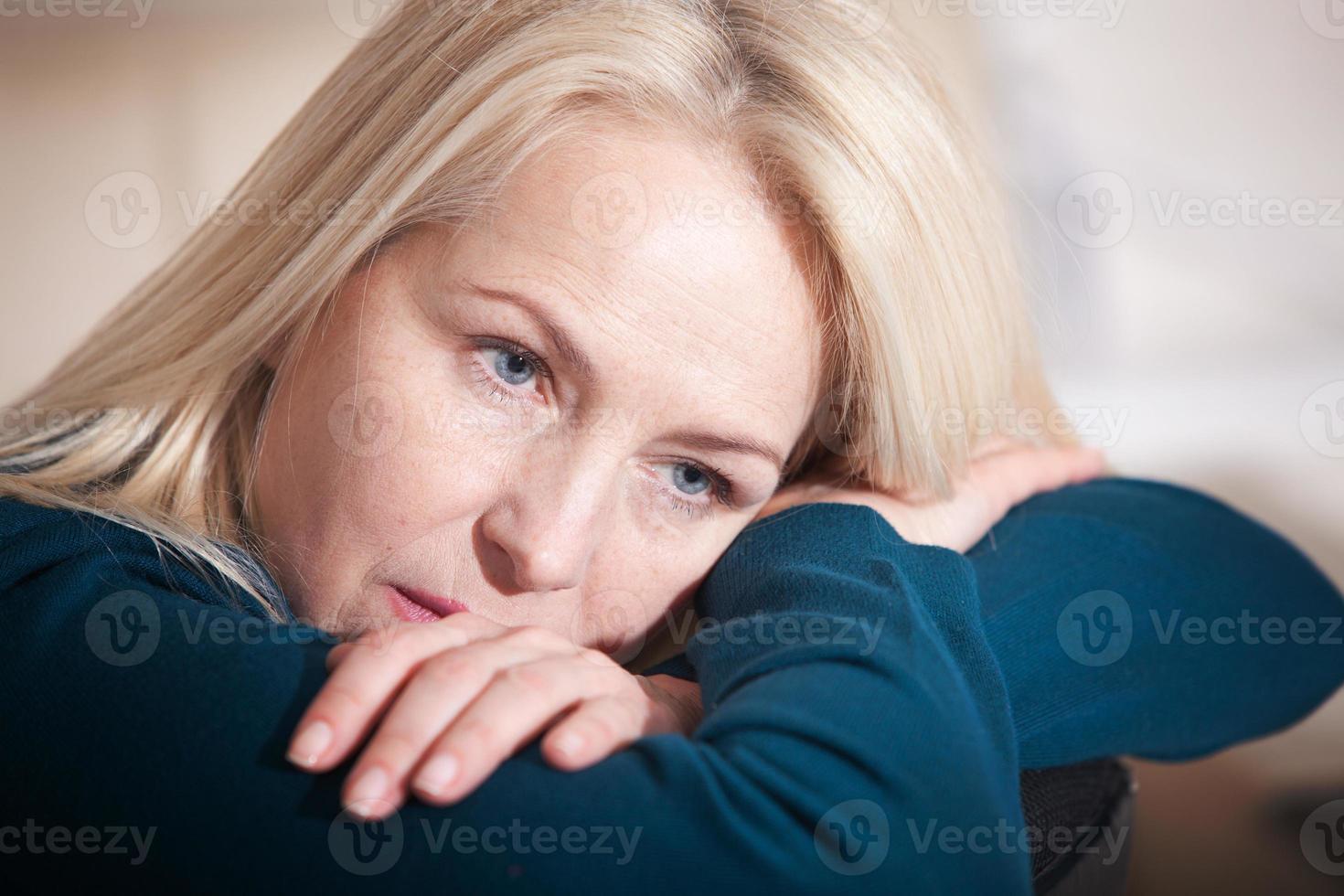 triste mujer deprimida de mediana edad en casa sentada en el sofá, mirando hacia abajo y tocando su frente, soledad y concepto de dolor foto