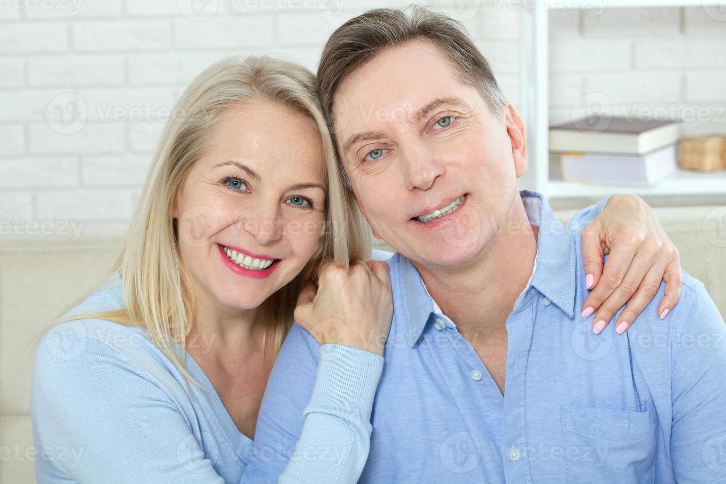 Middle aged couple relaxing on the couch smiling at camera at home in the living room photo