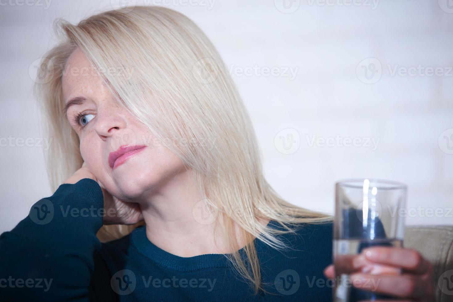 Woman drinking alcoholic concept of social problems sitting at home in a depressed state. Middle aged woman holding a glass asking for help. photo