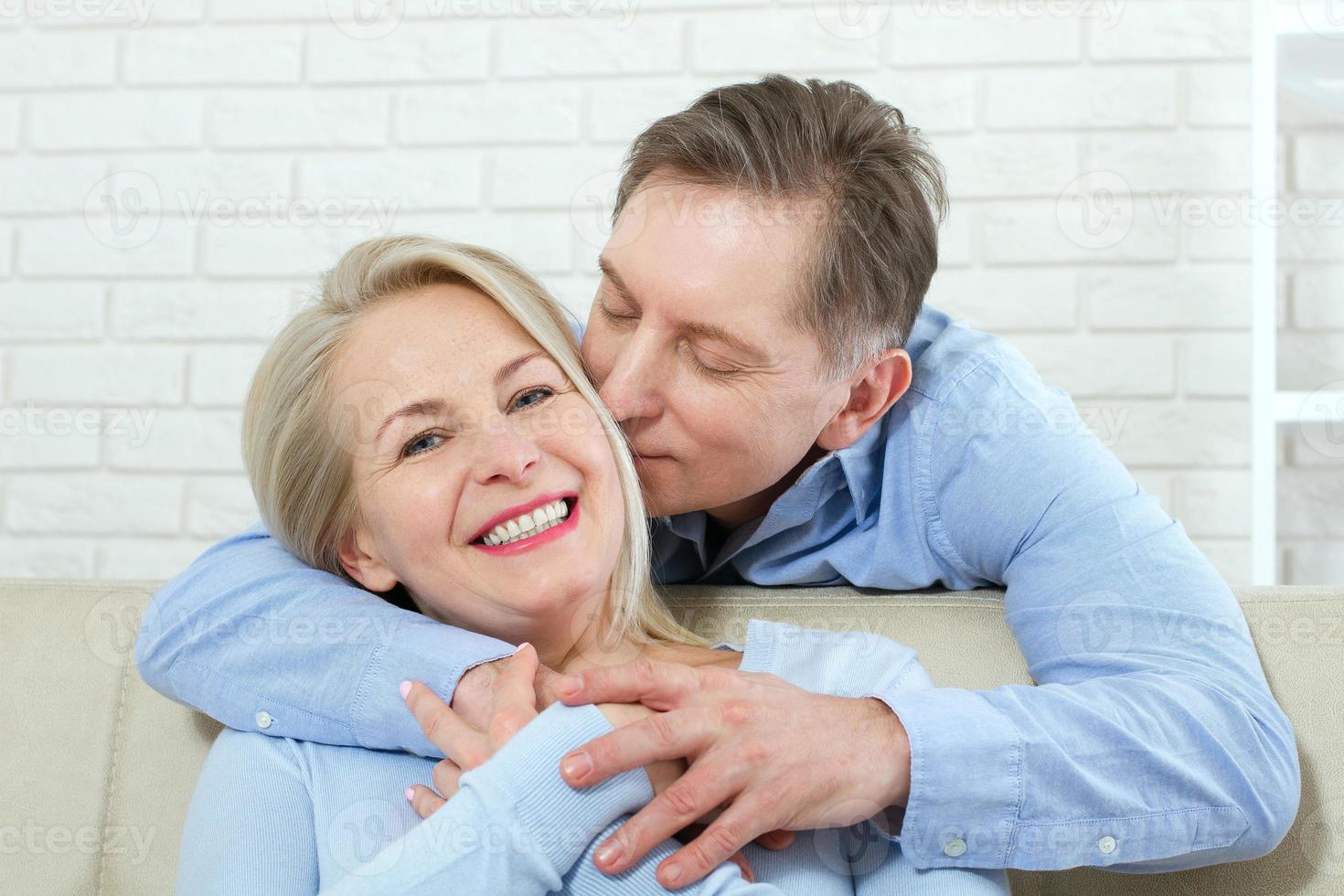 Close up photo of cheerful excited happy happily happy with toothy shining smile blond attractive woman and man, he hugs her from behind and kisses