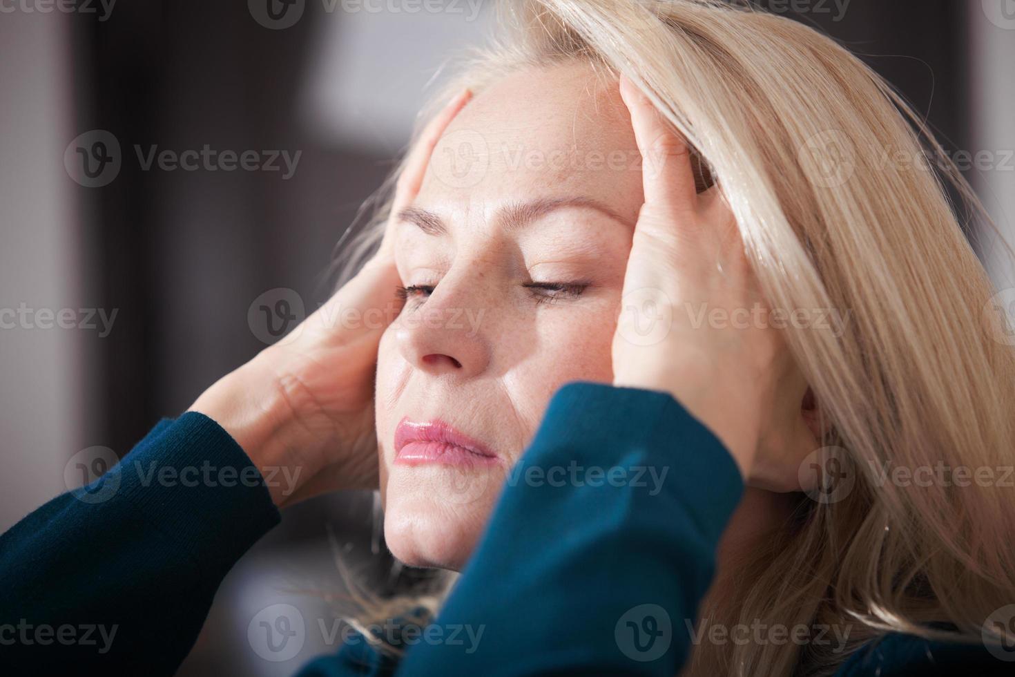 Middle aged woman barefoot sitting on the couch, hugging her head, at home. The concept of sadness and loneliness. photo