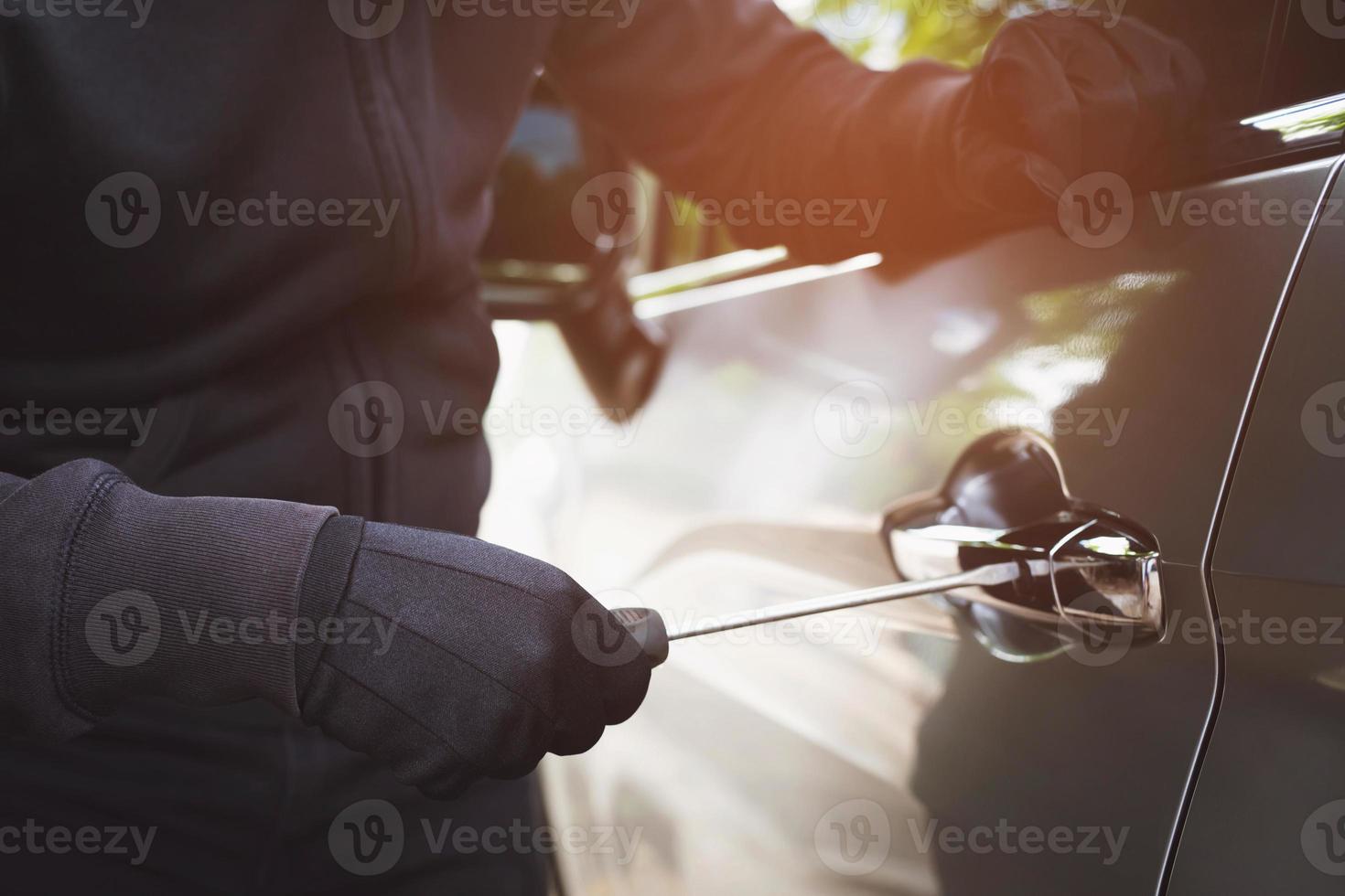 cierre la mano del ladrón de coches sujetando el destornillador y el guante negro robando el automóvil tratando de manejar la puerta para ver si el vehículo está desbloqueado tratando de entrar en el interior. foto