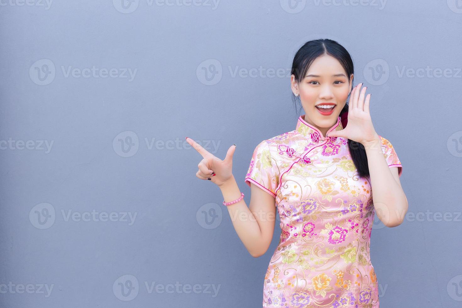 Beautiful Asian woman with long hair who wears pink Cheongsam dress in Chinese new year theme while her hand shows to present something and showing hand to point photo