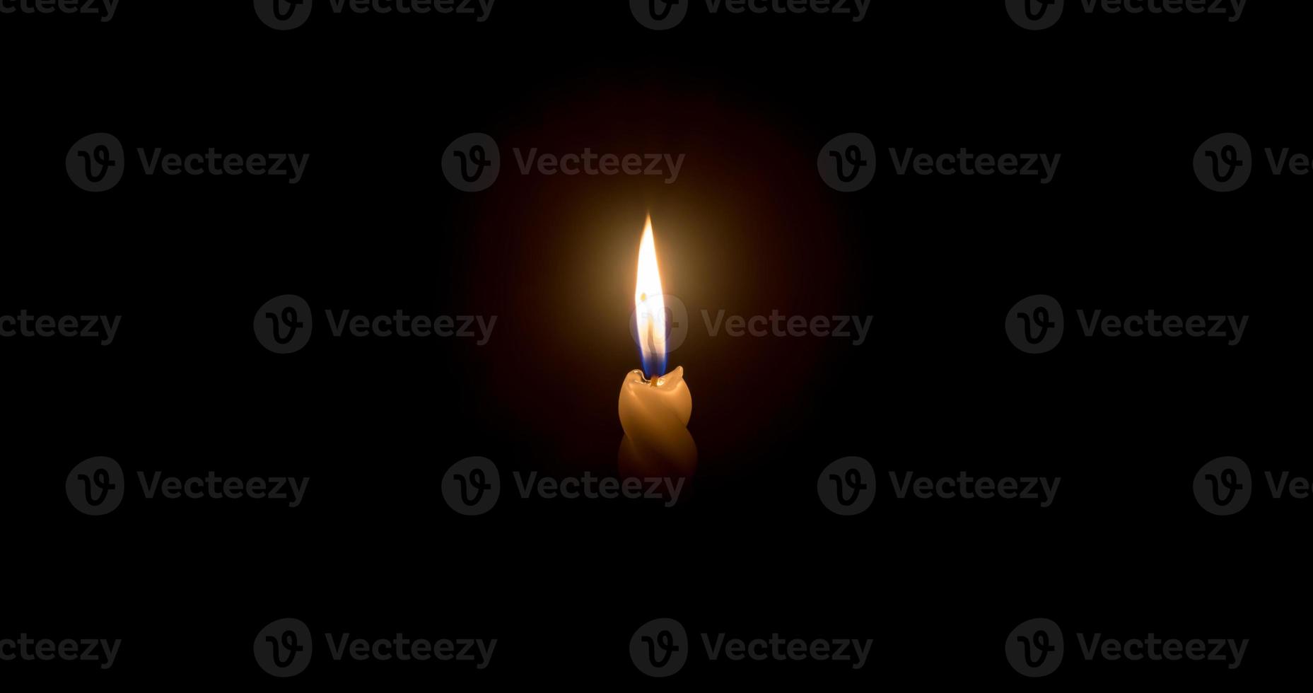 A single burning candle flame or light glowing on a spiral white candle on black or dark background on table in church for Christmas, funeral or memorial service photo