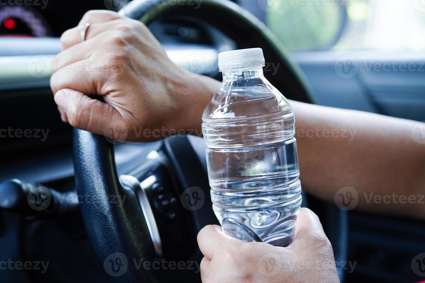 Asian woman driver hold cold water for drink in car, dangerous and risk an accident. photo