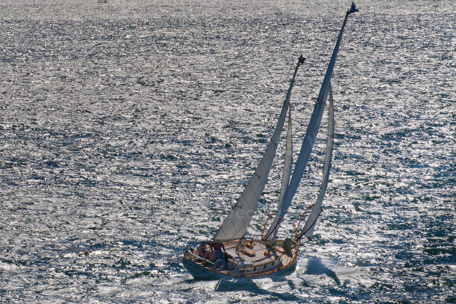 un barco de regata de madera con un capitán solitario navegando en el mar azul foto