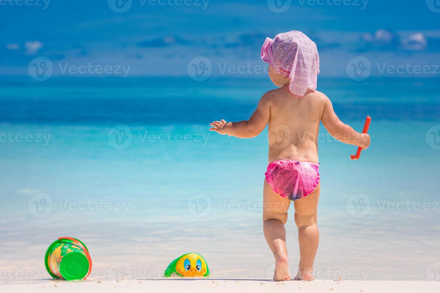 una niña pequeña y linda está jugando en una playa cerca del mar. adorable niña pequeña jugando con juguetes de playa en la playa de arena blanca, vacaciones familiares de lujo, vistas exóticas a la playa foto