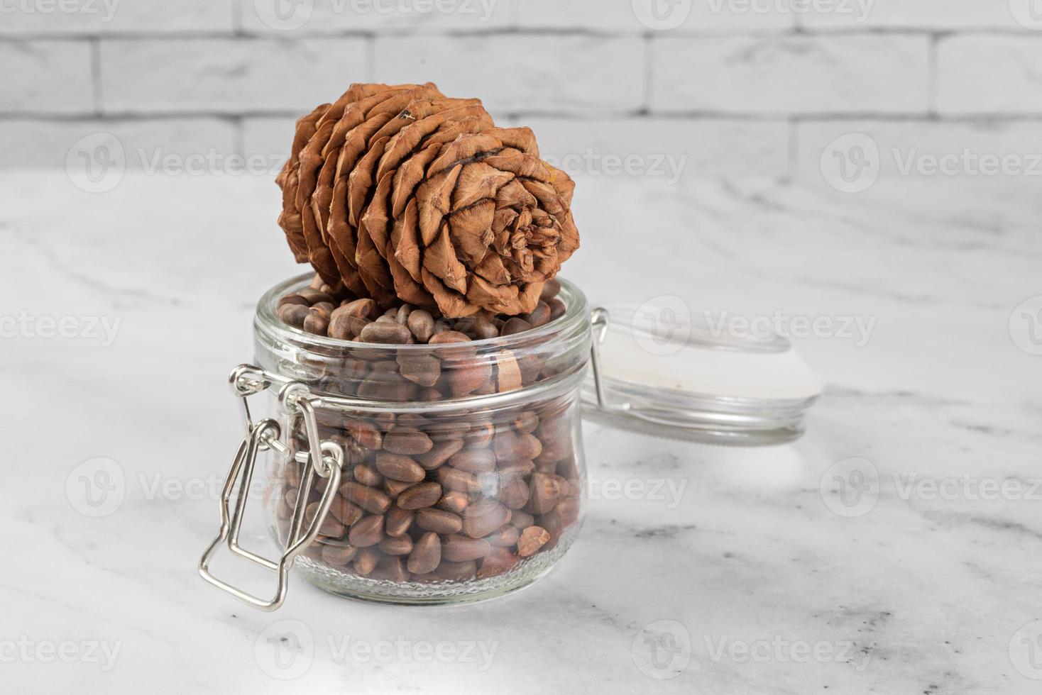 Pine nuts in a jar and a pine cone in the kitchen on a light background. photo