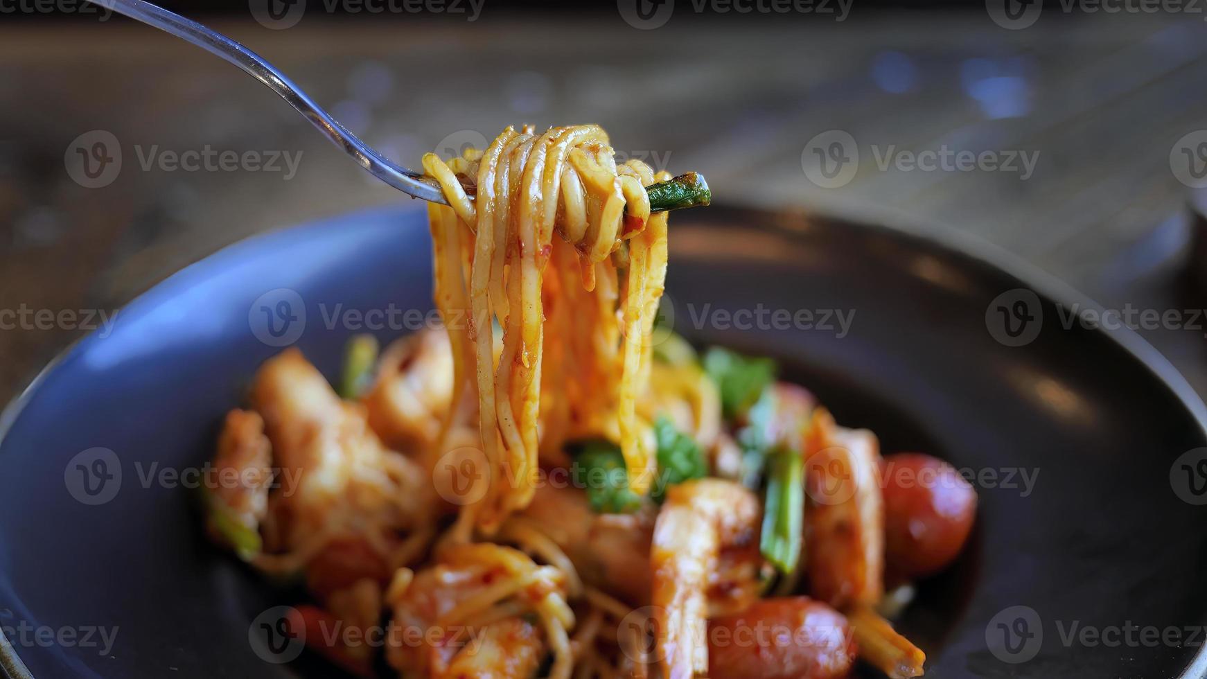 Close up, selective focus, Italian pasta spaghetti with prawns in Tom Yum flavor, Thai style pasta, tasty and spicy, delicious menu in dark color plate on wooden table photo