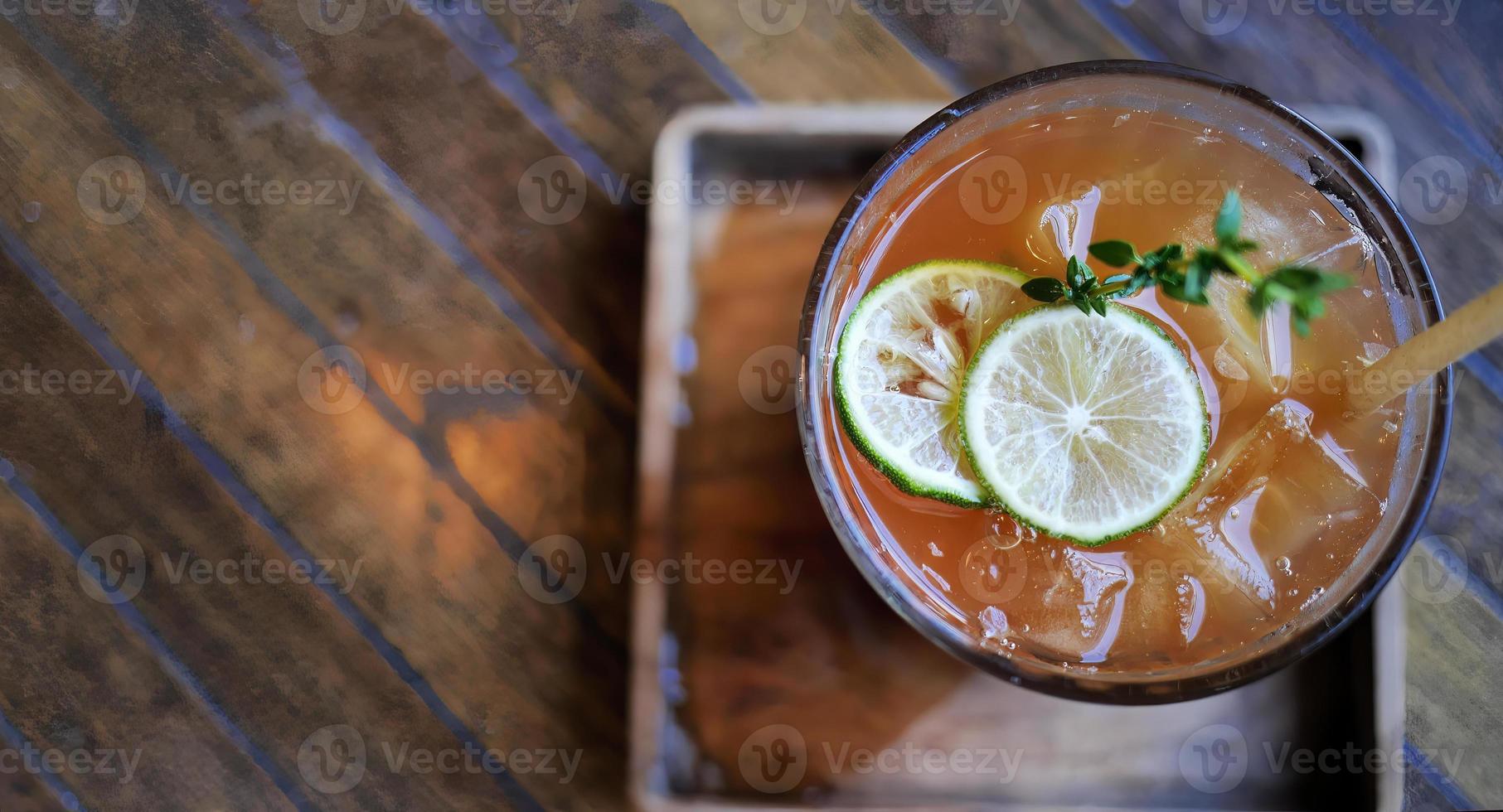 Directly above view, Selective focus a glass of refreshing cold soft drink lemon iced tea in ice cube with paper straw, decorated with sliced lime and thyme branches, summer drink photo