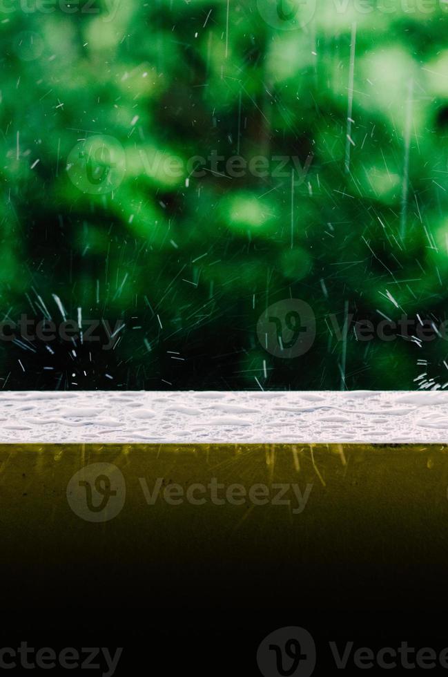 toma cinematográfica de gotas de lluvia que caen del cielo gris y sobre la superficie húmeda de la baranda de un balcón, creando ondas en el agua quieta foto