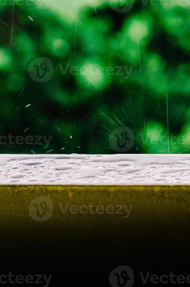 Cinematic shot of raindrops falling from the grey skies and onto the wet surface of a balcony railing, creating ripples in the still water photo
