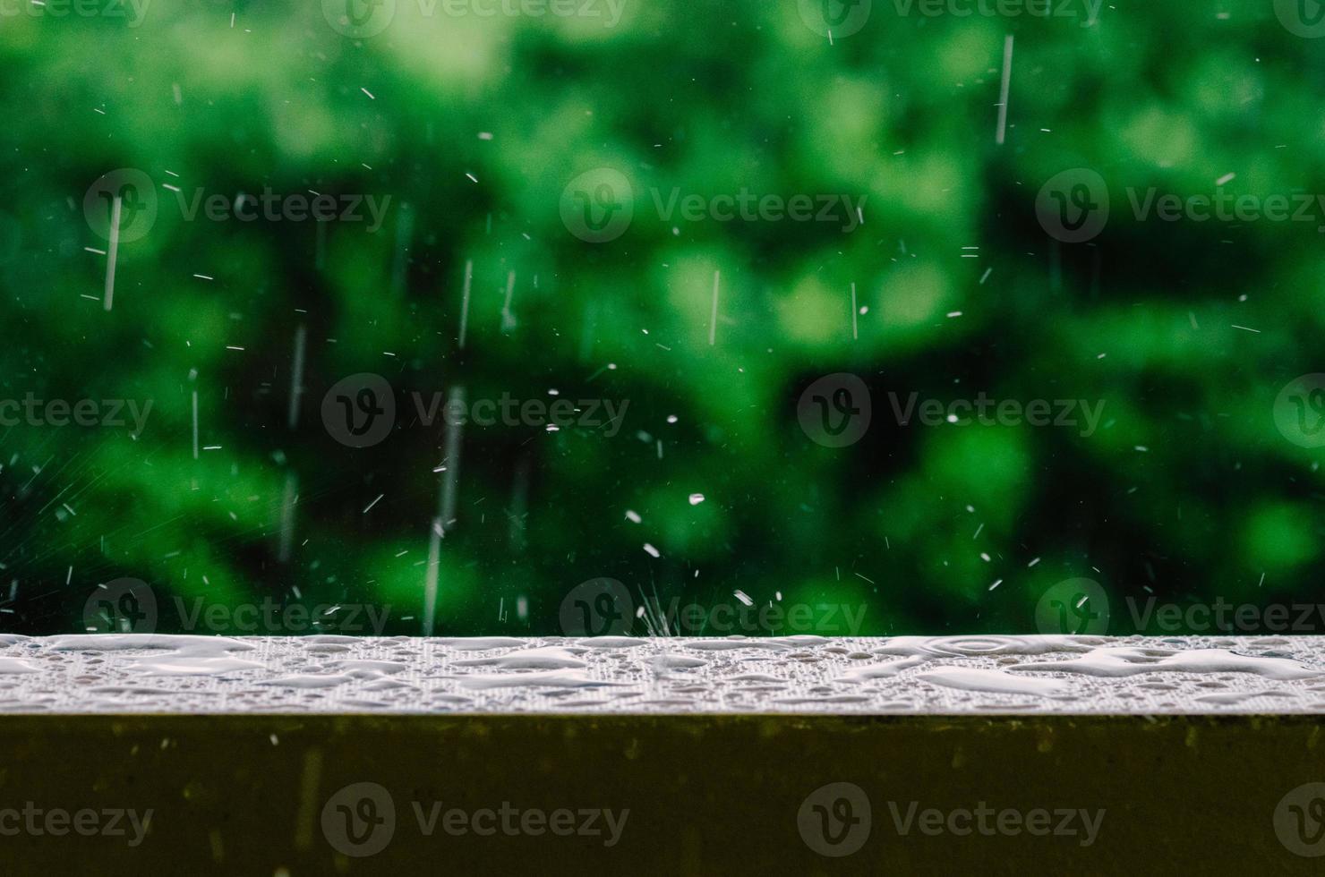 Cinematic shot of raindrops falling from the grey skies and onto the wet surface of a balcony railing, creating ripples in the still water photo