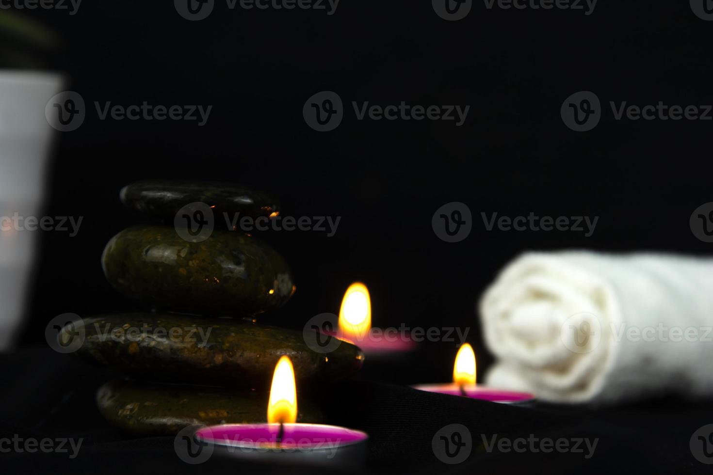 Layers of stones are on dark background, two rounded candles with white towel, use for massage and yoga obect concepts. photo