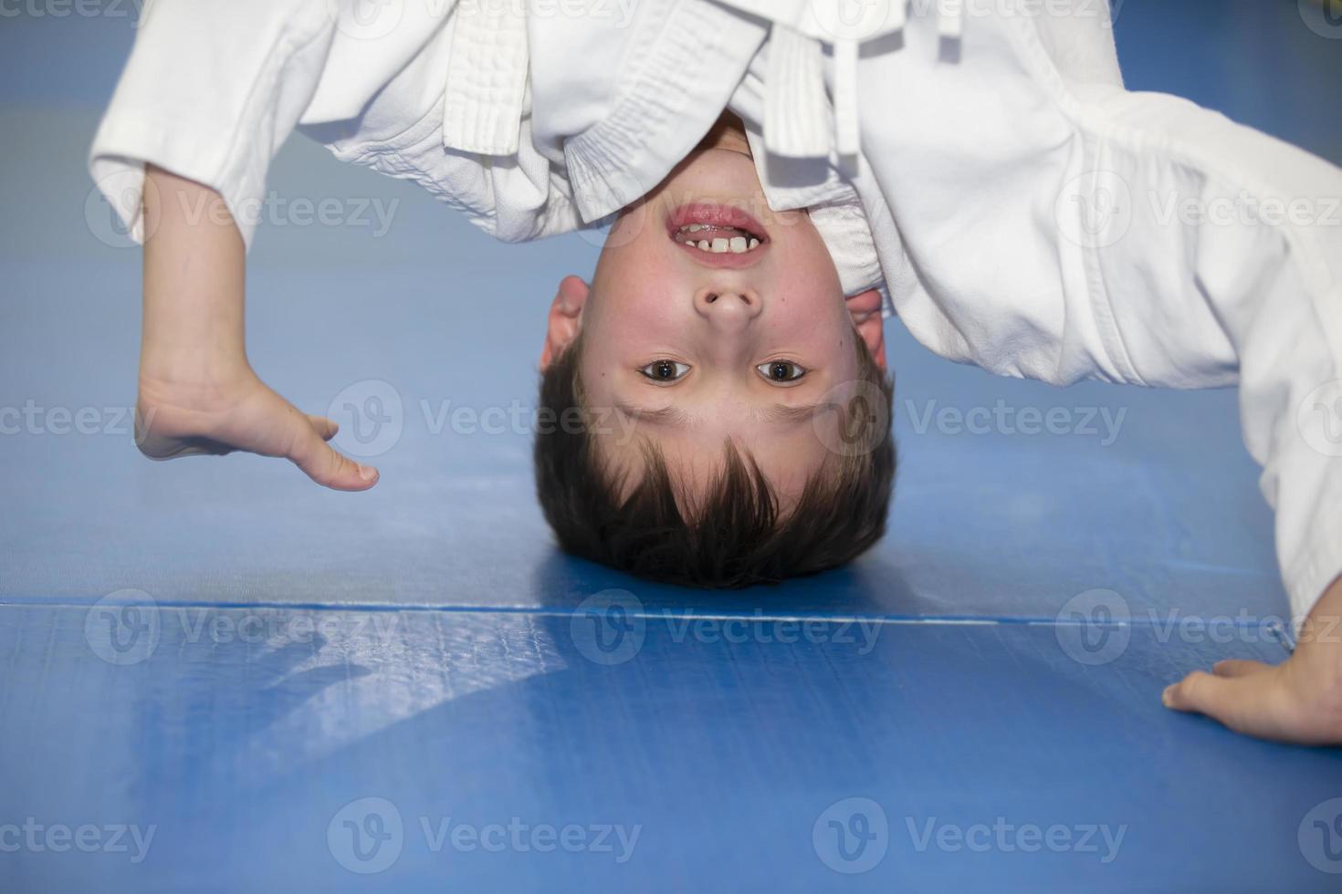 A small boy in a kimano upside down. The child is engaged in judo or karate. Section for children of combat sports. photo