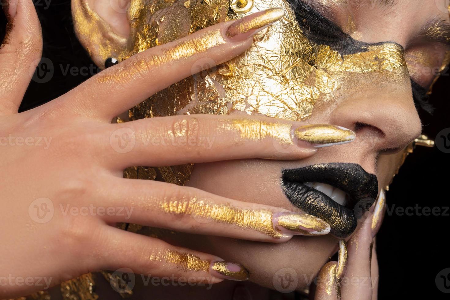 Beauty fashion model girl with golden make-up and body on black background. Golden body art. The golden face of a beautiful lady is touching. Artistic portrait. photo