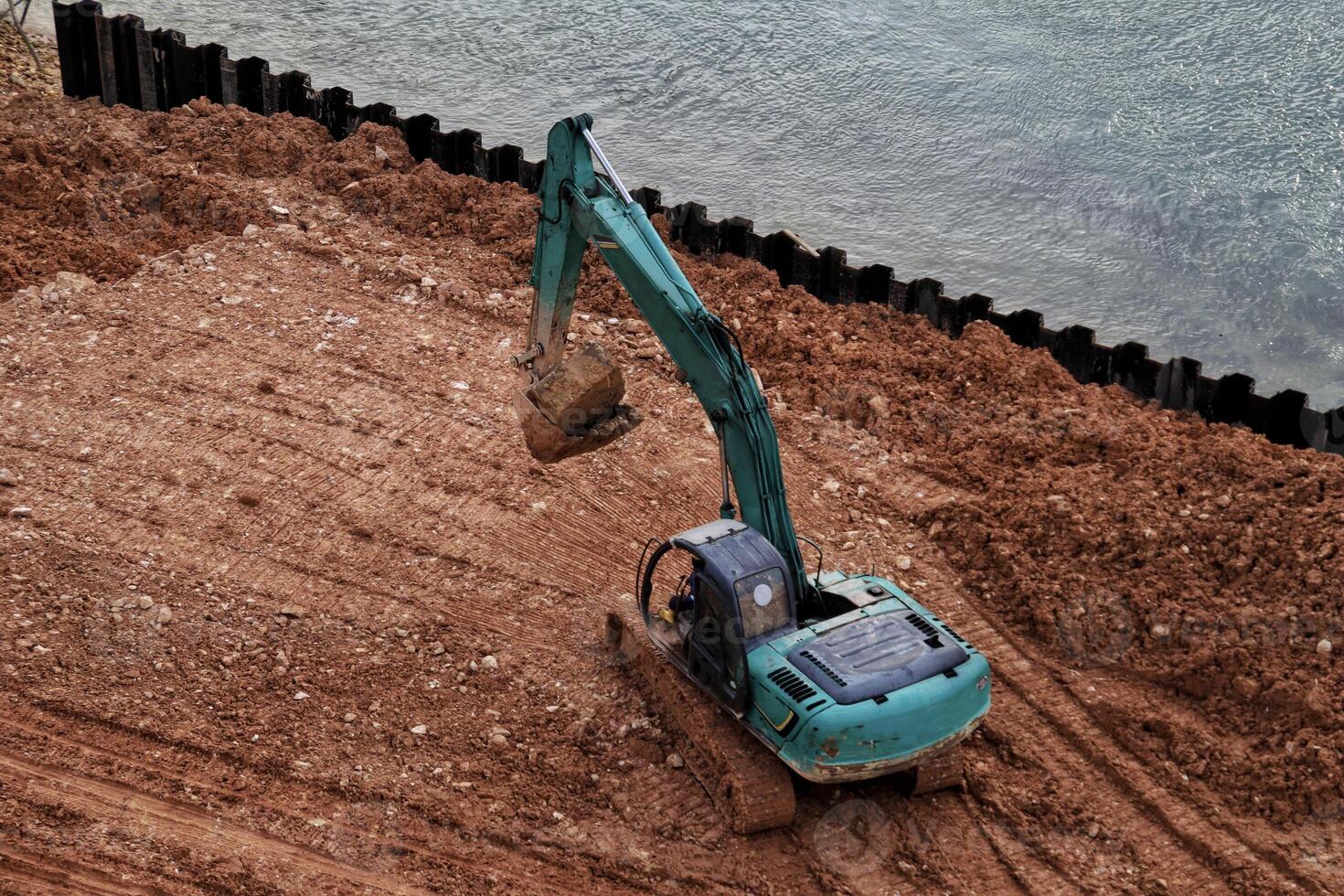 Green excavator flatten the ground near the water or the river. photo